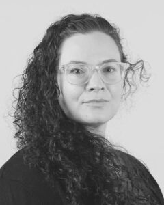Kelsie Acton is a white woman with glasses and lots of curly hair.