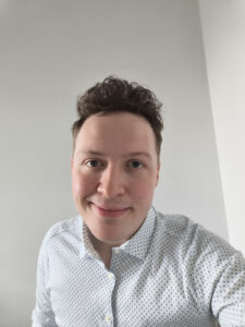 Gu&eth;ni is white with short dark hair. He is wearing a white shirt and smiling.