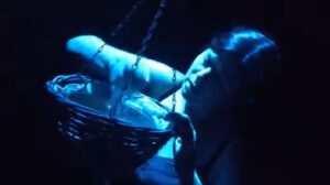 Kathy is a white woman with dark hair. She is lit with blue light and scooping water from a bowl.